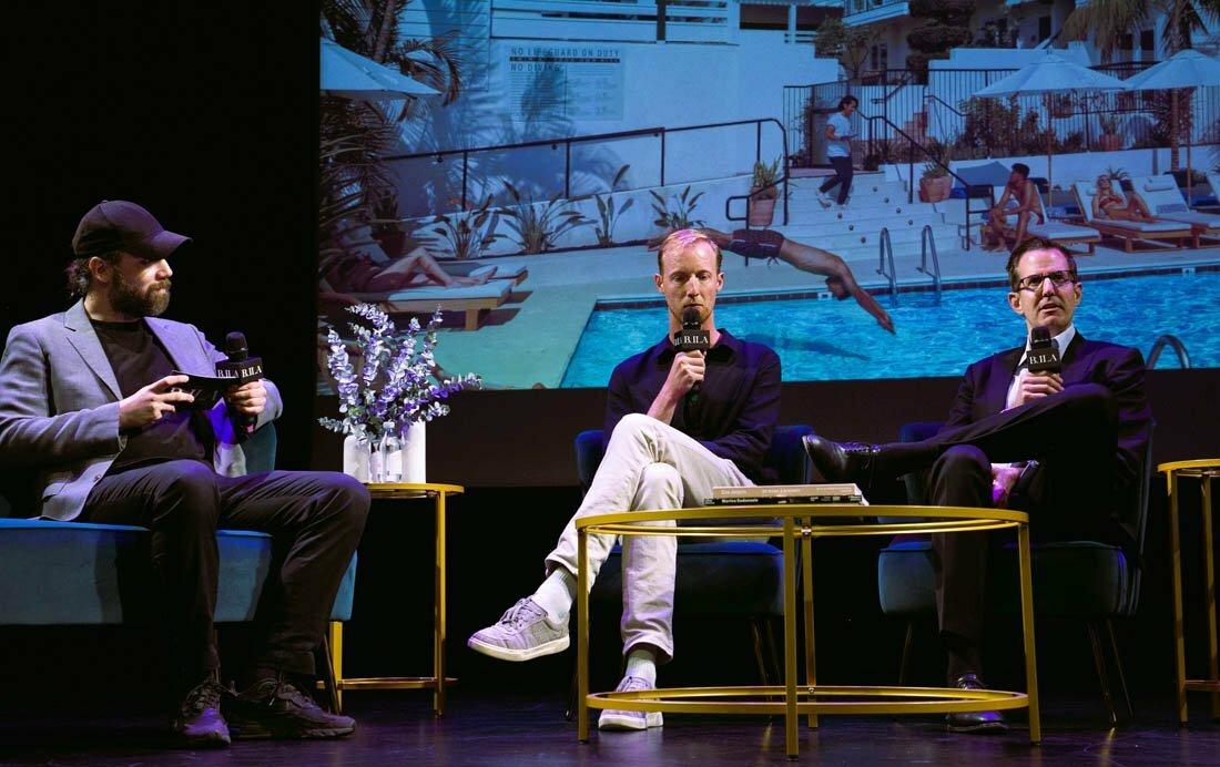 Three panelists with BHIA microphones on stage, a poolside hotel scene projected behind them