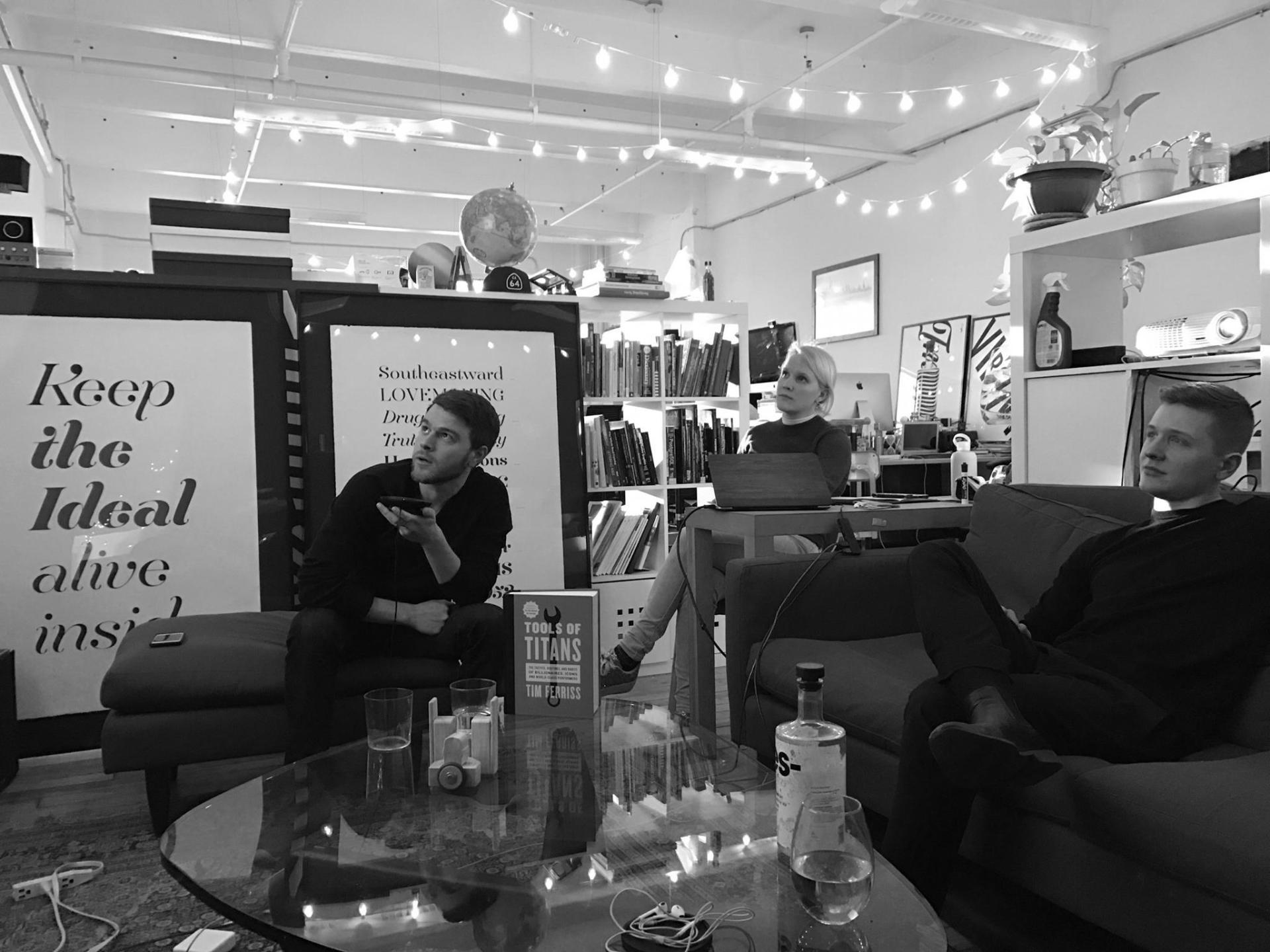 Three people talking in L+R's lounge among bookshelves, framed prints and string lights