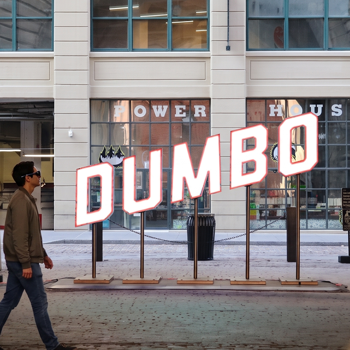 Man wearing smart glasses walks past the large DUMBO sign in Brooklyn
