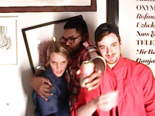 Three people posing for the camera at an indoor party, one holding out a drink