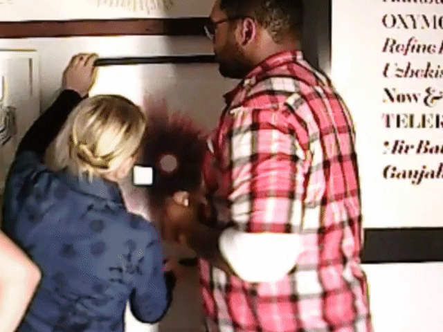 Three people crowded against a wall of framed prints at an indoor party