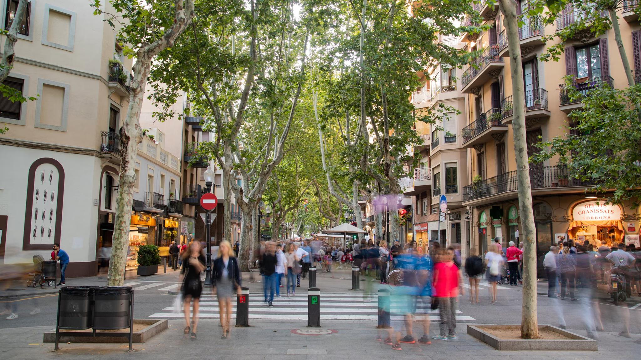 Tree-lined pedestrian street with shops, cafes, and blurred people walking