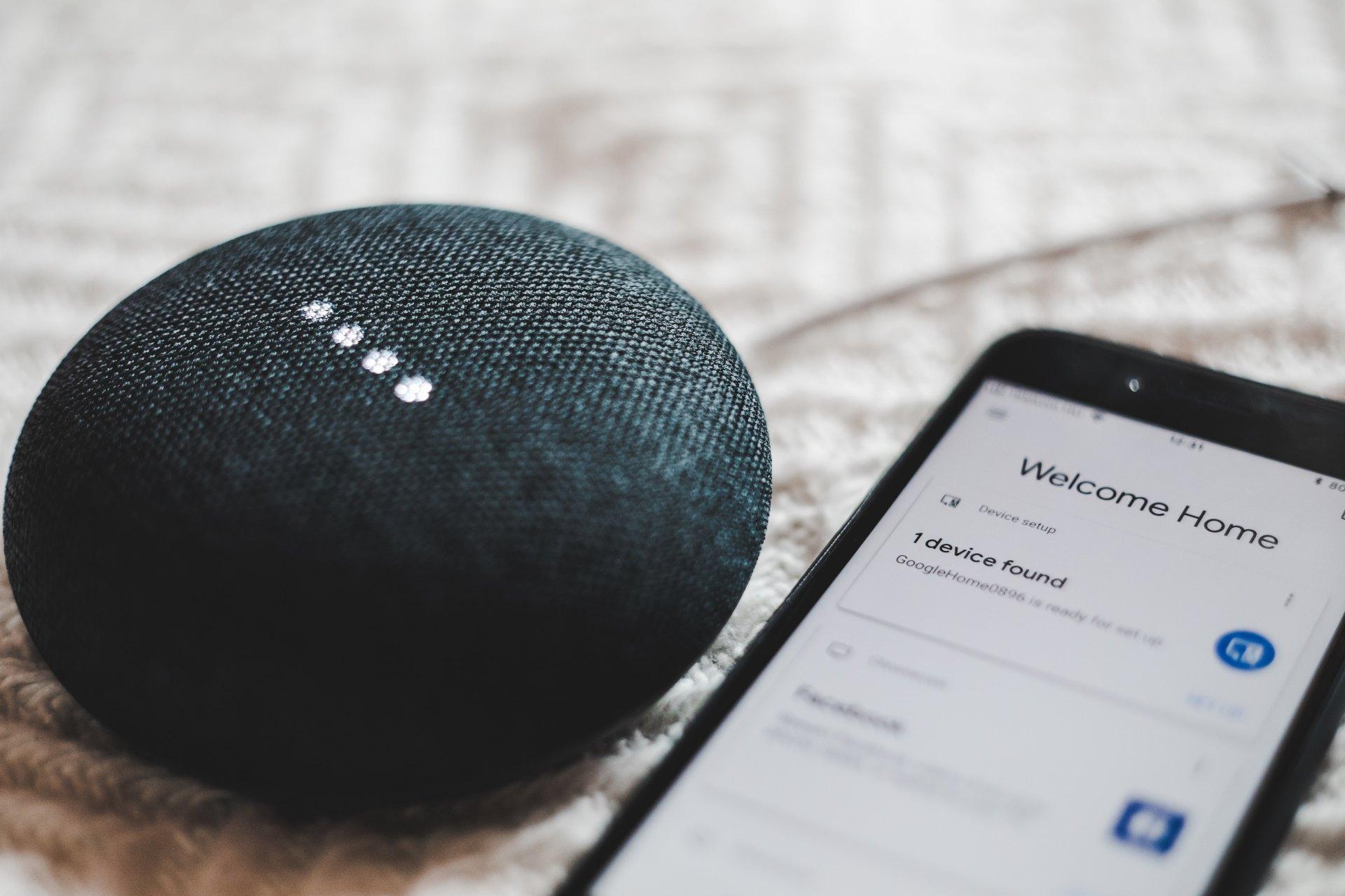 Google Home Mini speaker beside a phone running device setup and reporting one device found