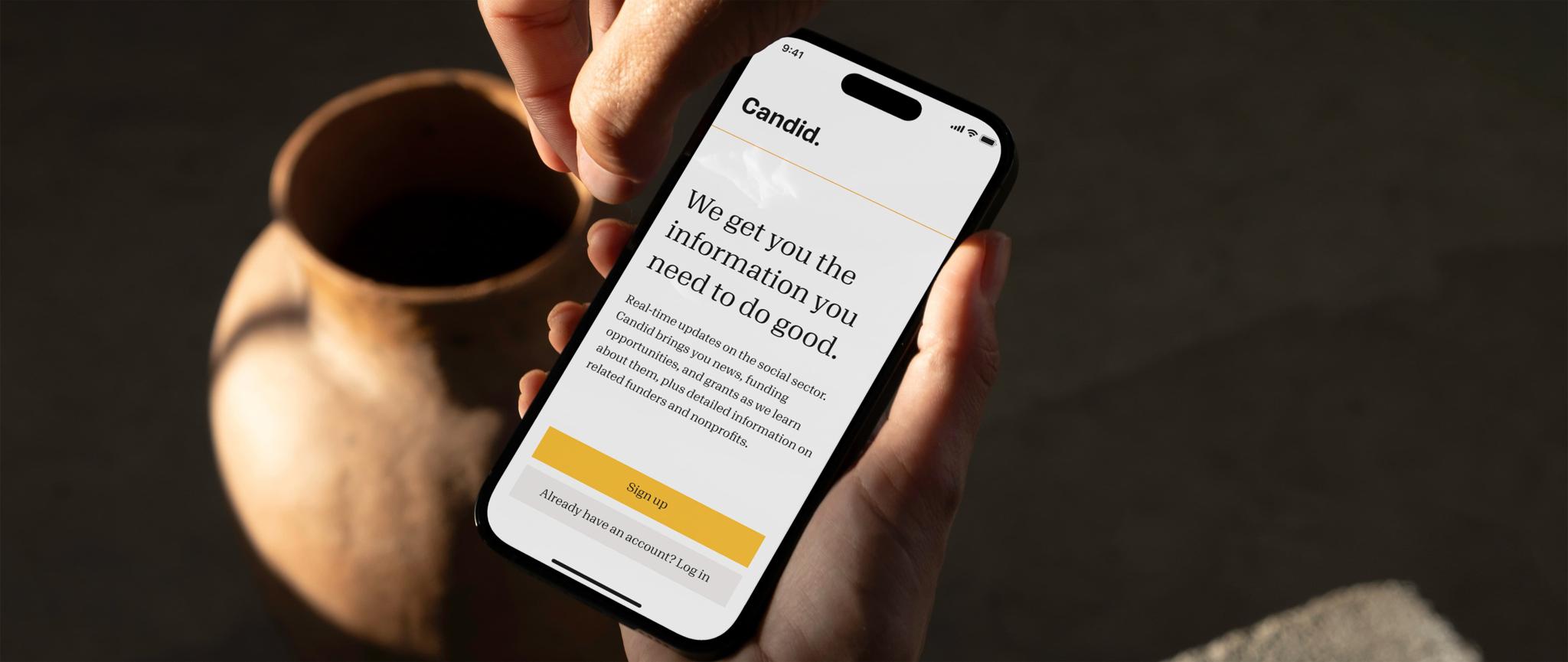 Hand holding a phone with the Candid sign-up page open beside a ceramic vase