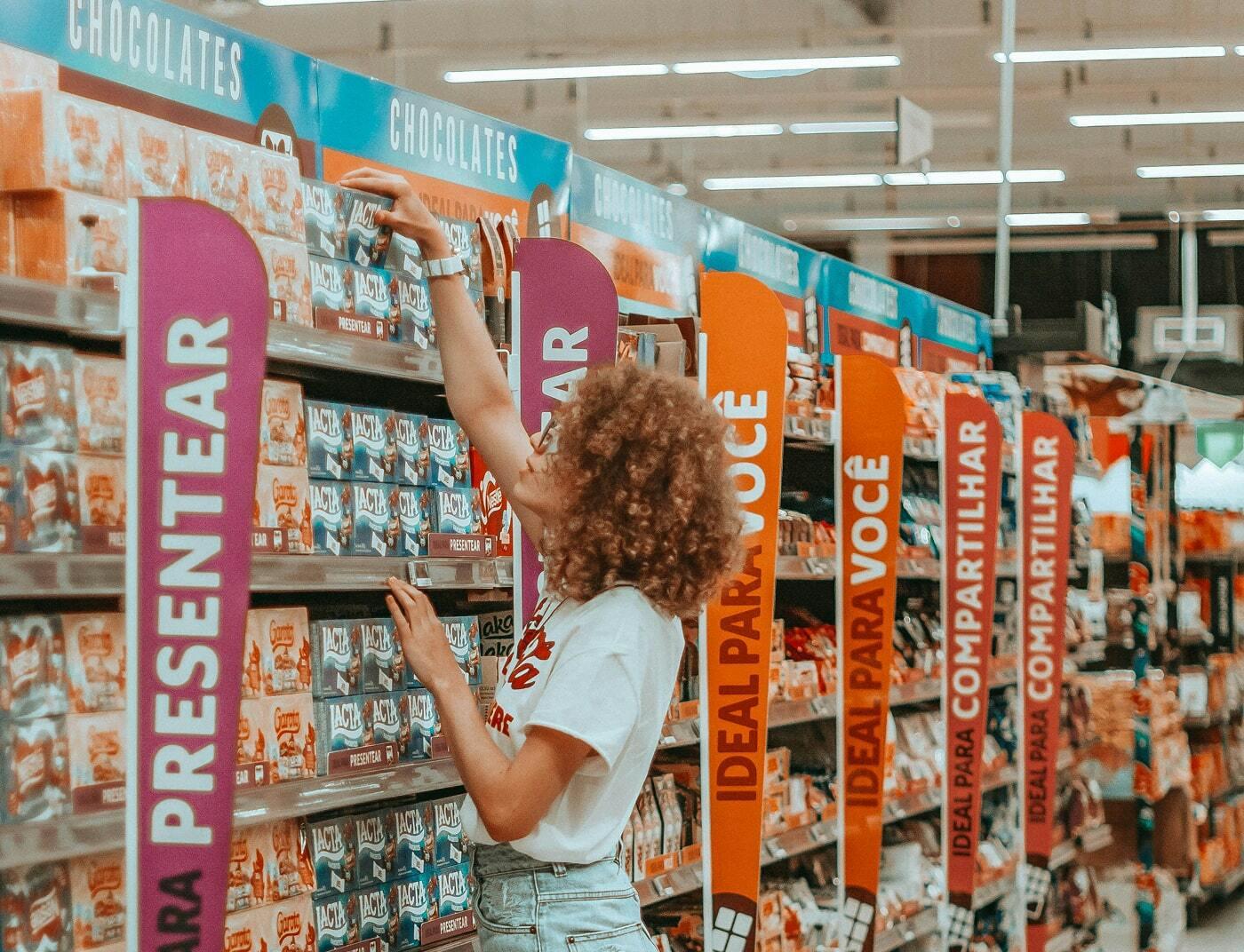 Shopper reaching for chocolate boxes in a supermarket aisle with Portuguese promotional signage