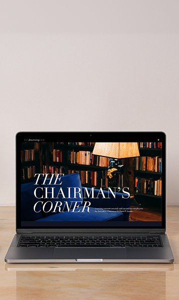 Laptop on a desk displaying The Chairman's Corner webpage with a library scene.