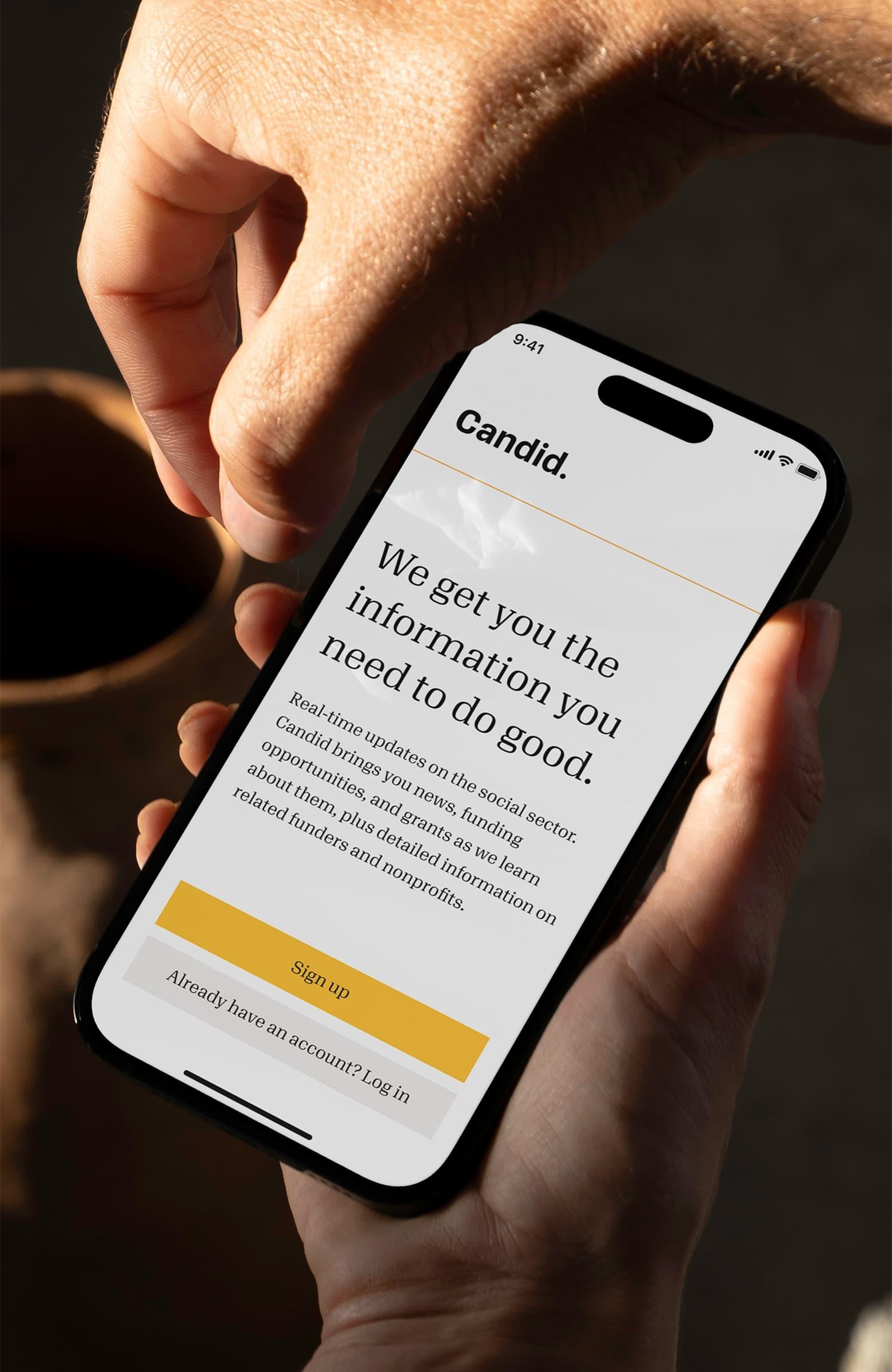 Hand holding a phone with the Candid sign-up page open beside a ceramic vase