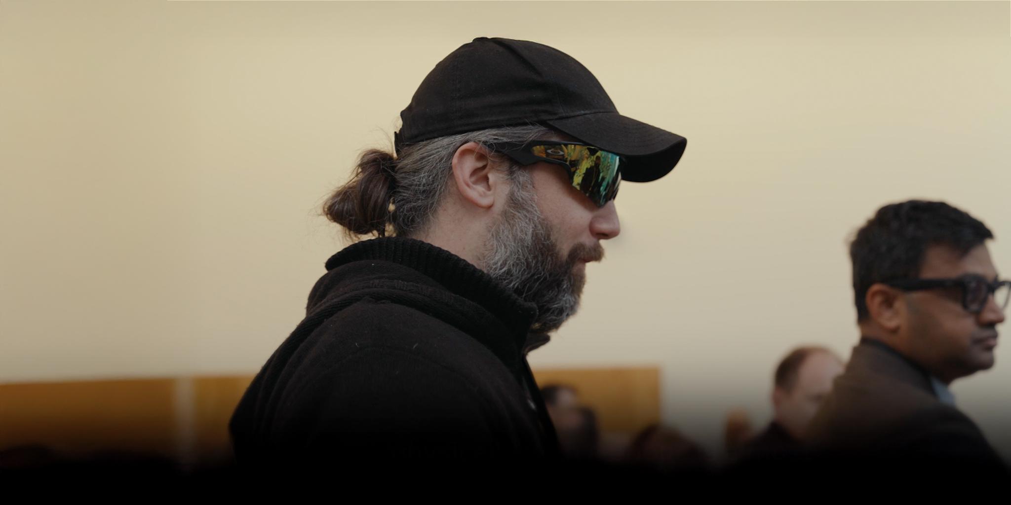 Man in a black cap and sunglasses shown in profile