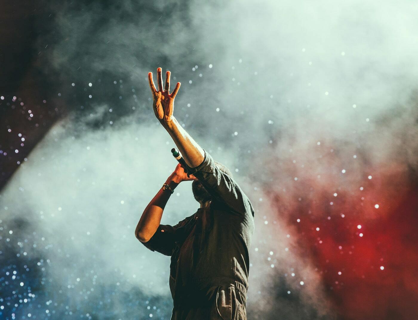 Performer with arms raised in a cloud of coloured stage smoke