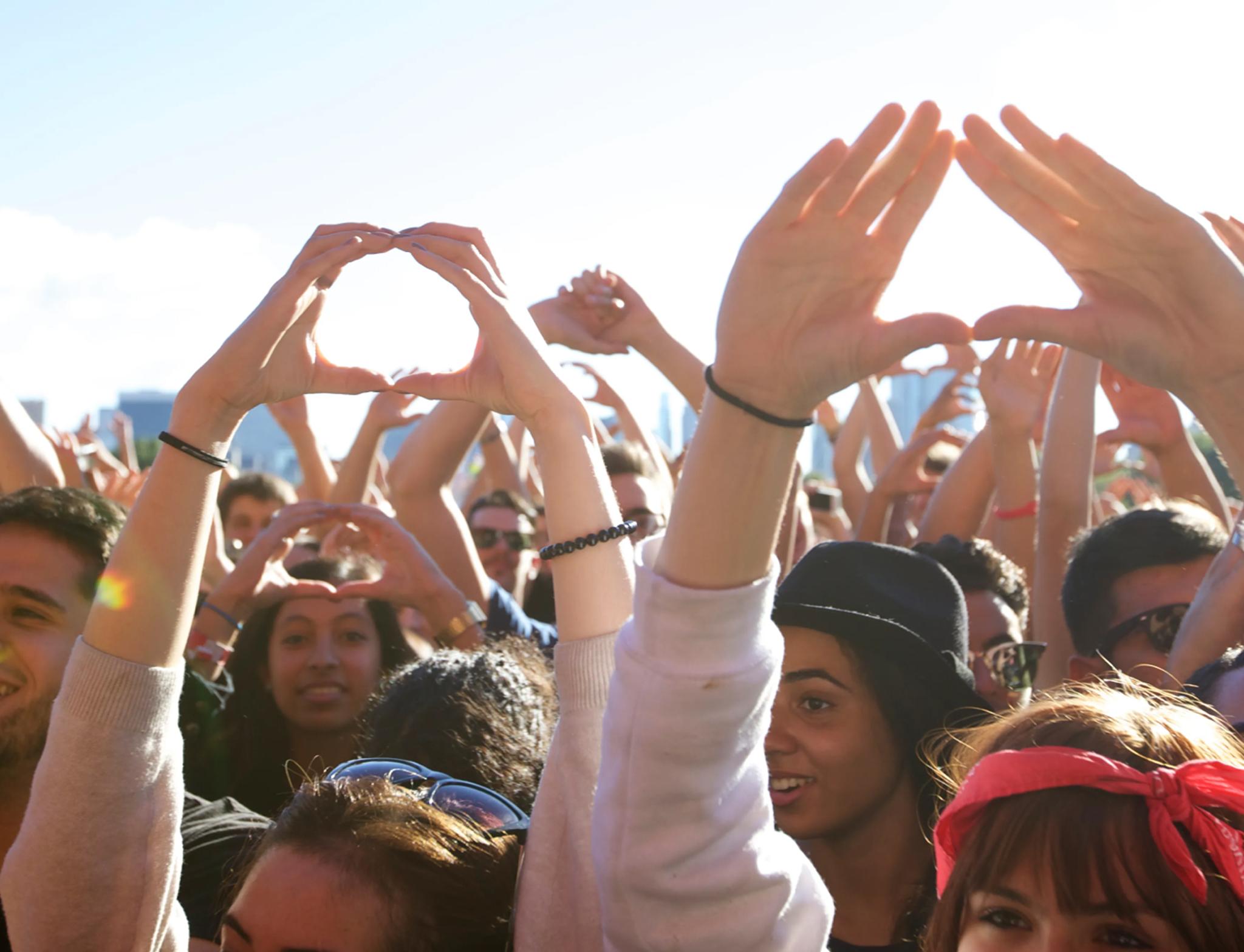 Festival crowd with raised hands forming heart shapes in sunlight