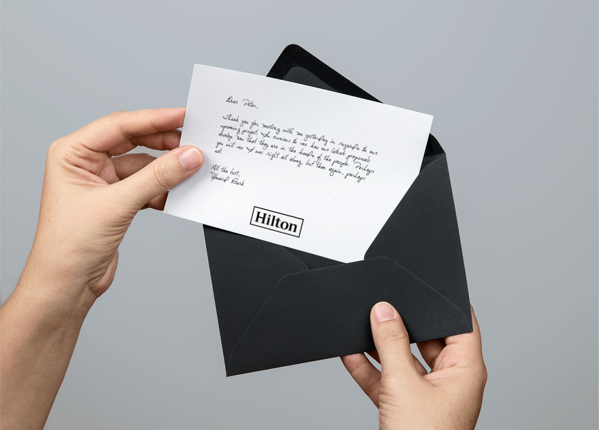 Hands pulling a handwritten Hilton note from a black envelope
