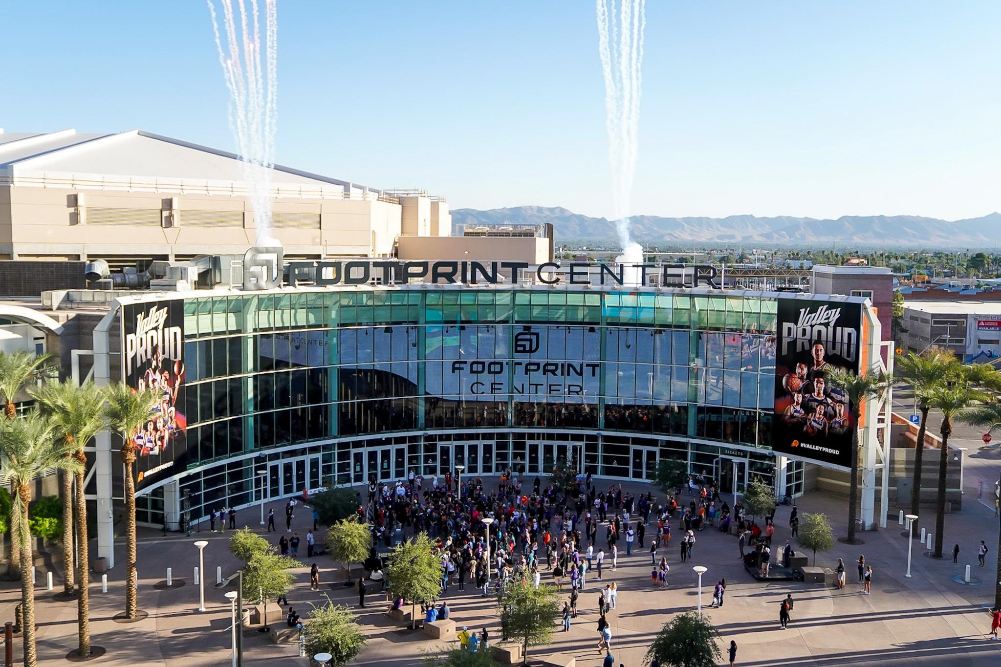 Crowds outside Footprint Center in Phoenix as firework smoke trails rise above the arena roof