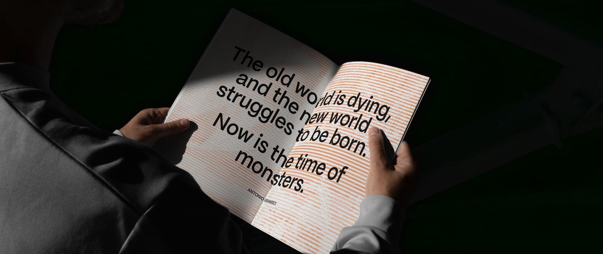 Hands holding an open book spread with the Antonio Gramsci quote about the old world dying