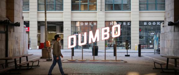 Dumbo Hero Desktop Man in smart glasses walks past the illuminated DUMBO sign outside Powerhouse Books