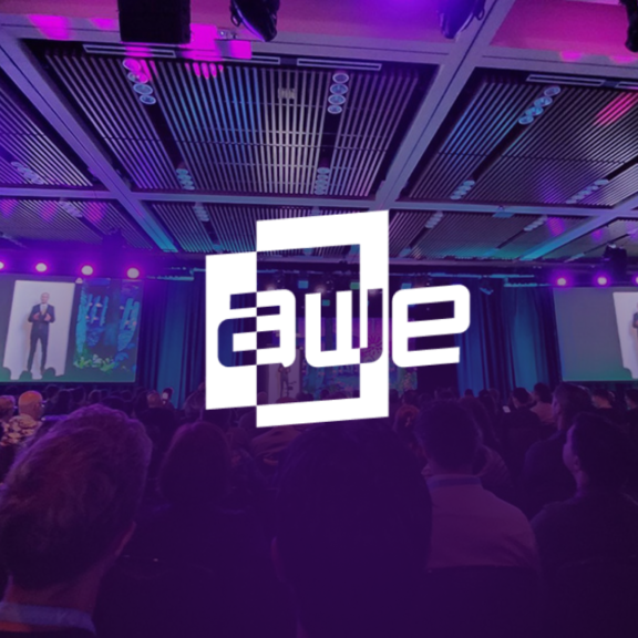 AWE logo over a conference audience with purple stage lighting