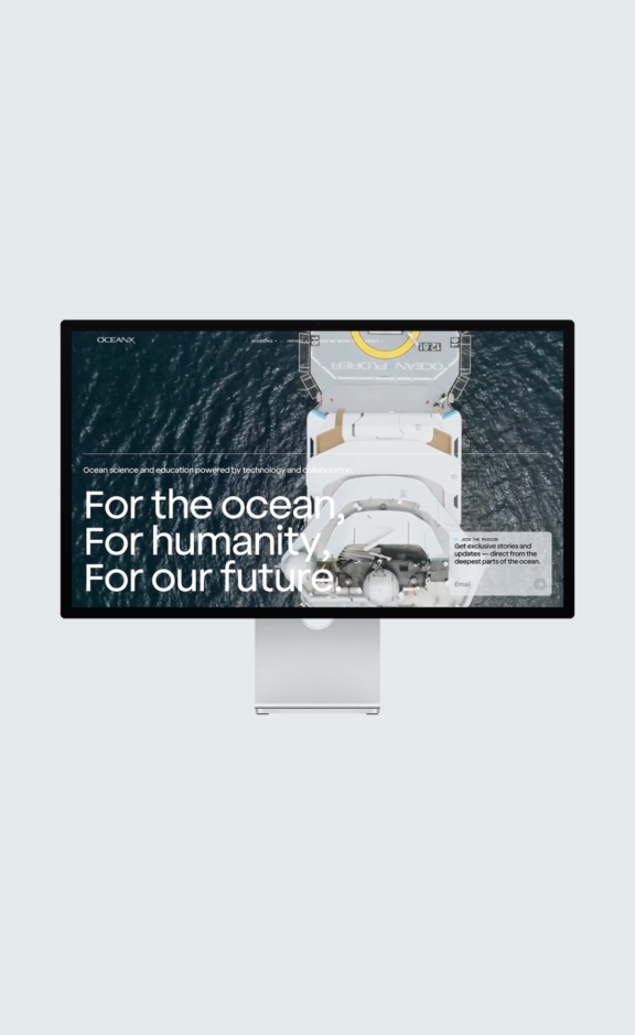 Ocean X M Cover Desktop monitor displaying an OceanX homepage over an aerial boat photo
