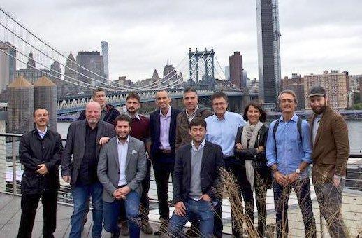 Group of visiting business leaders on a Brooklyn rooftop with the Manhattan Bridge behind them