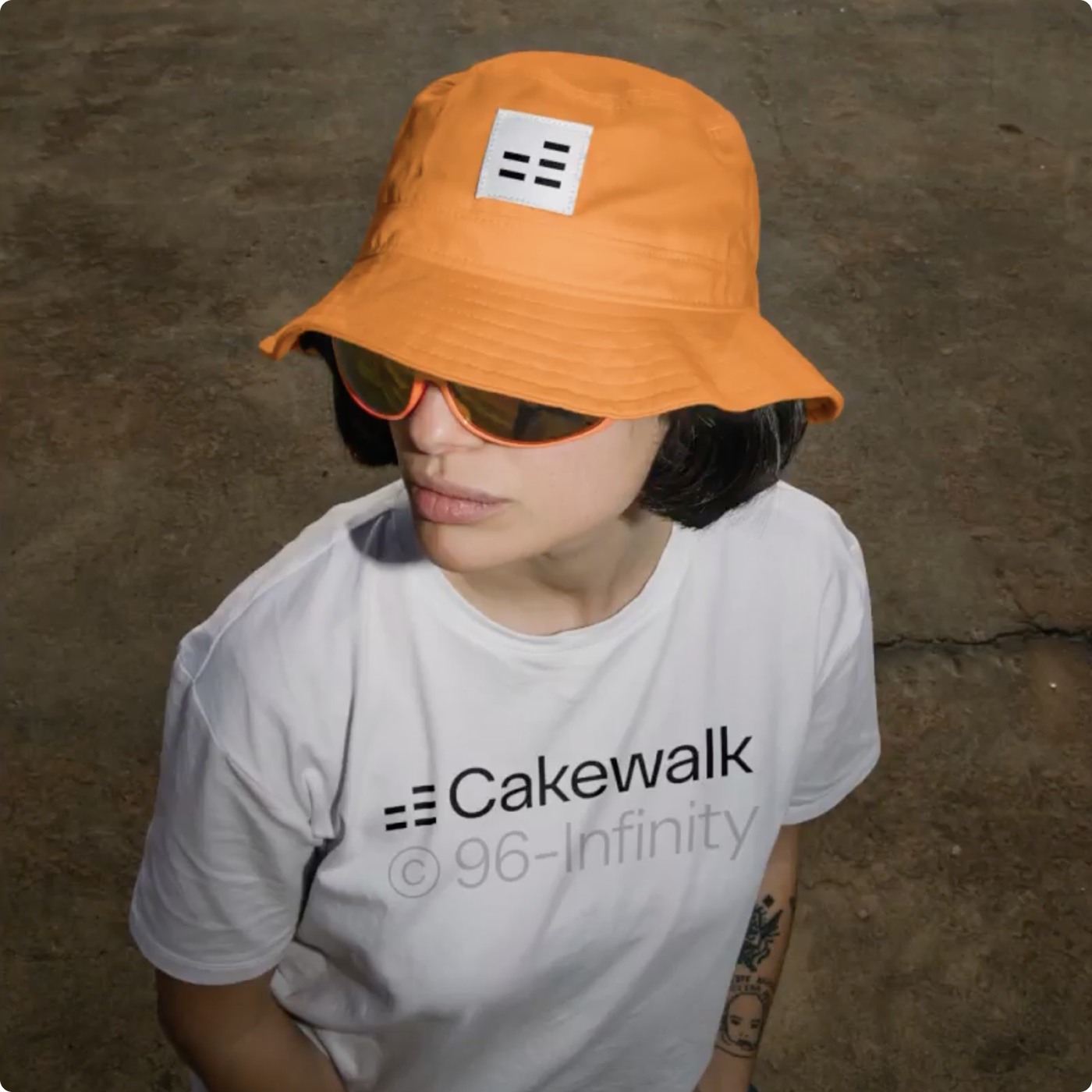 Person wearing orange bucket hat, sunglasses, and white Cakewalk T-shirt on concrete floor