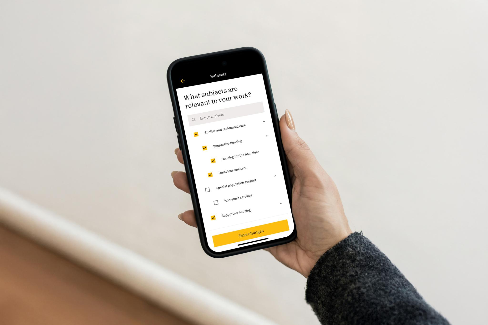 Hand holding a phone with the Candid subject preferences screen for shelter and housing