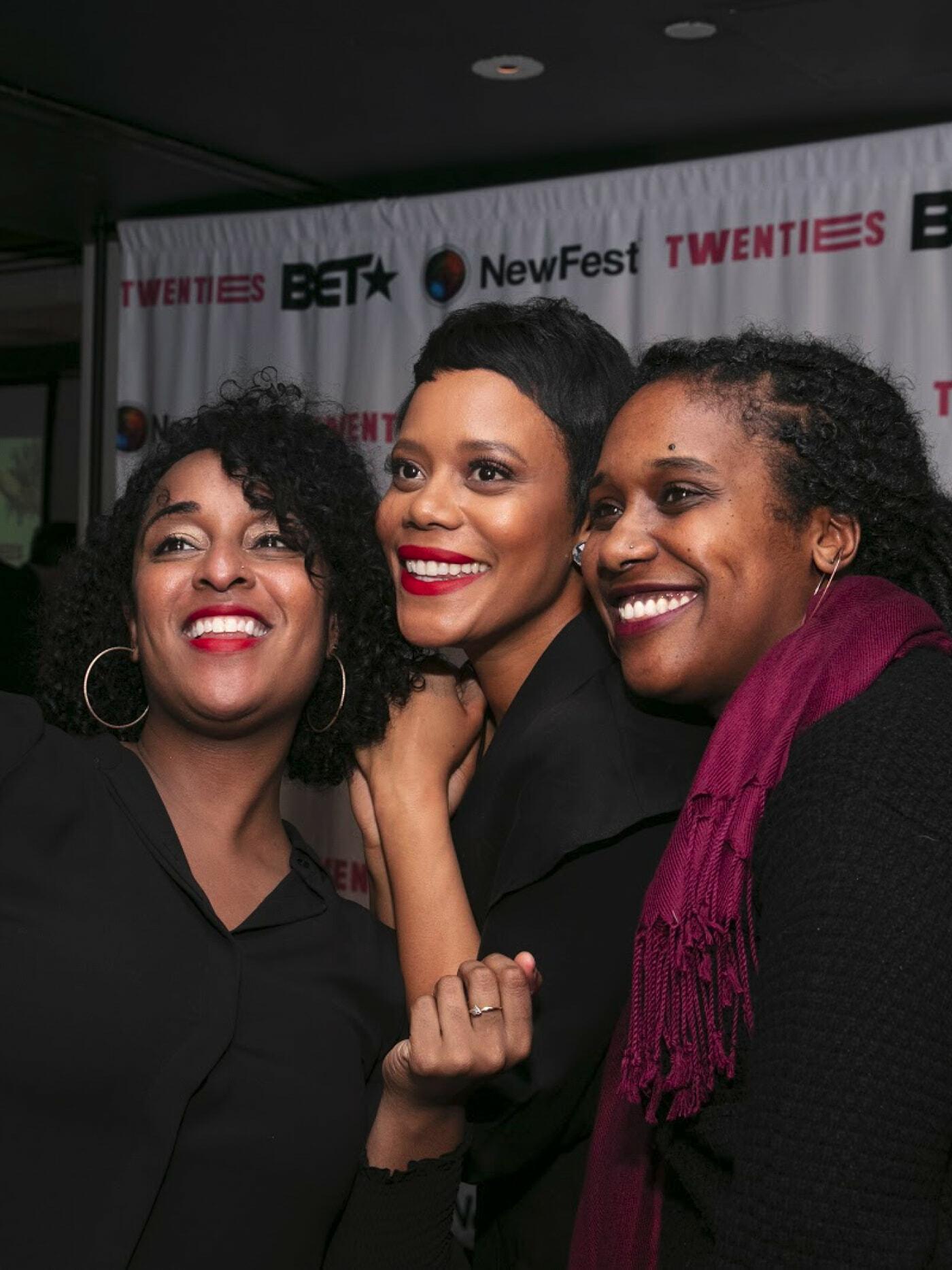 Three attendees smiling at a NewFest step-and-repeat with BET and Twenties branding