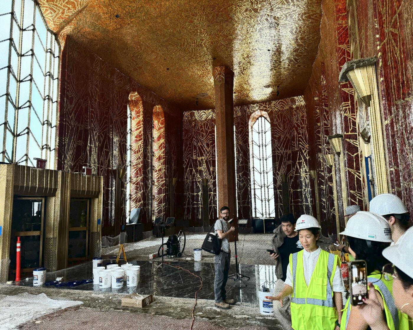 Construction site inside an ornate hall with workers in hard hats and temporary lighting.