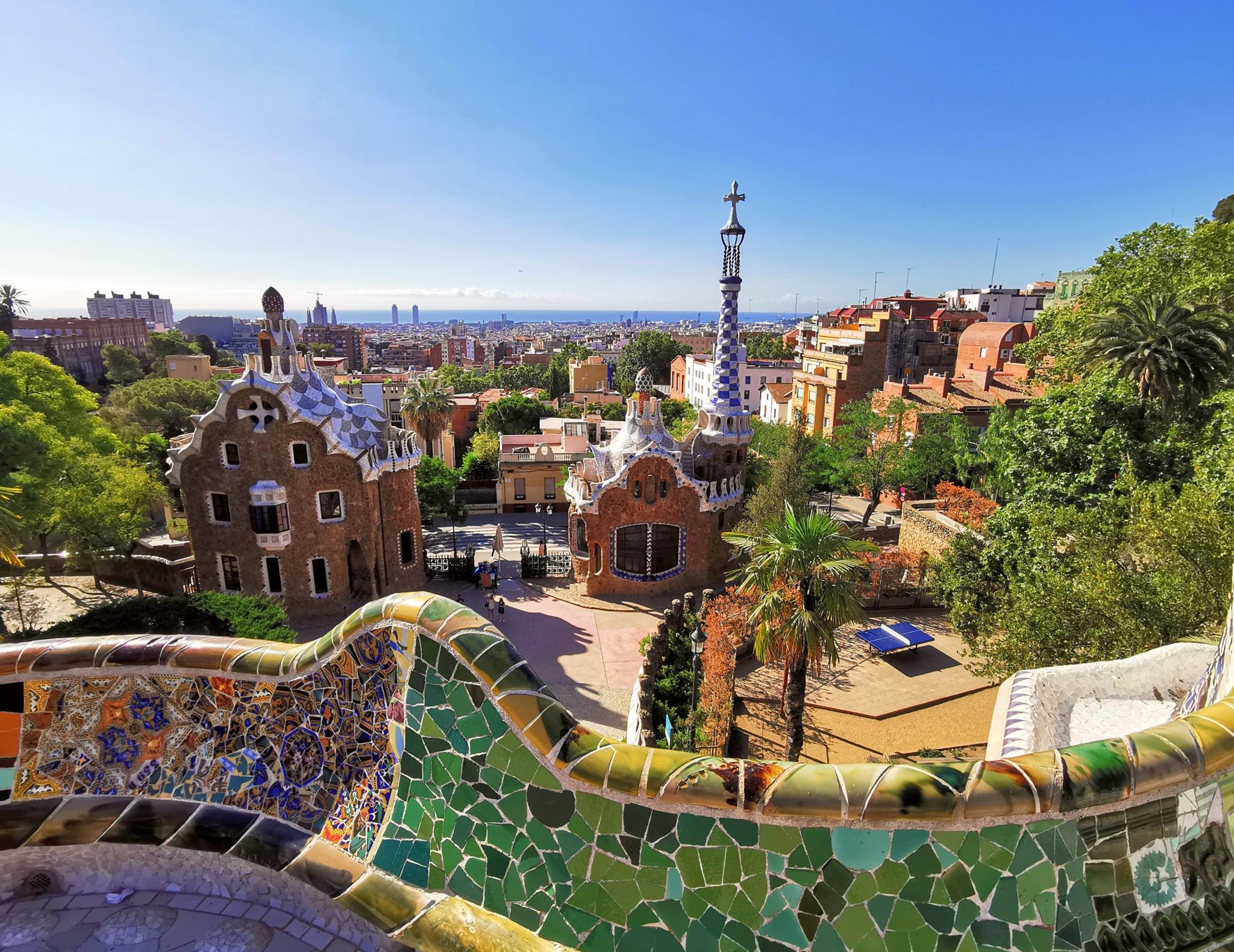 View over Park Guell in Barcelona from its mosaic terrace, with the city and sea beyond.