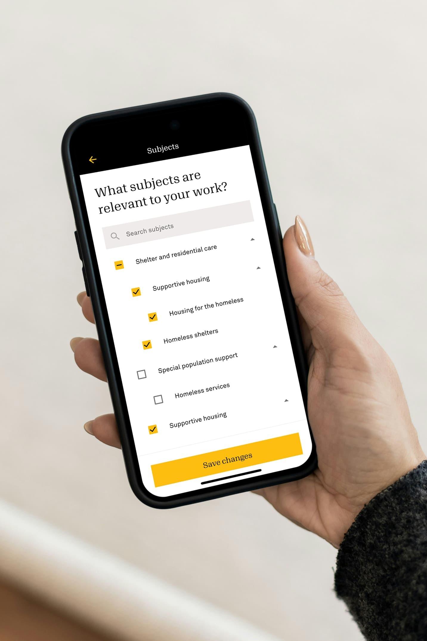 Hand holding a phone with the Candid subject preferences screen for shelter and housing
