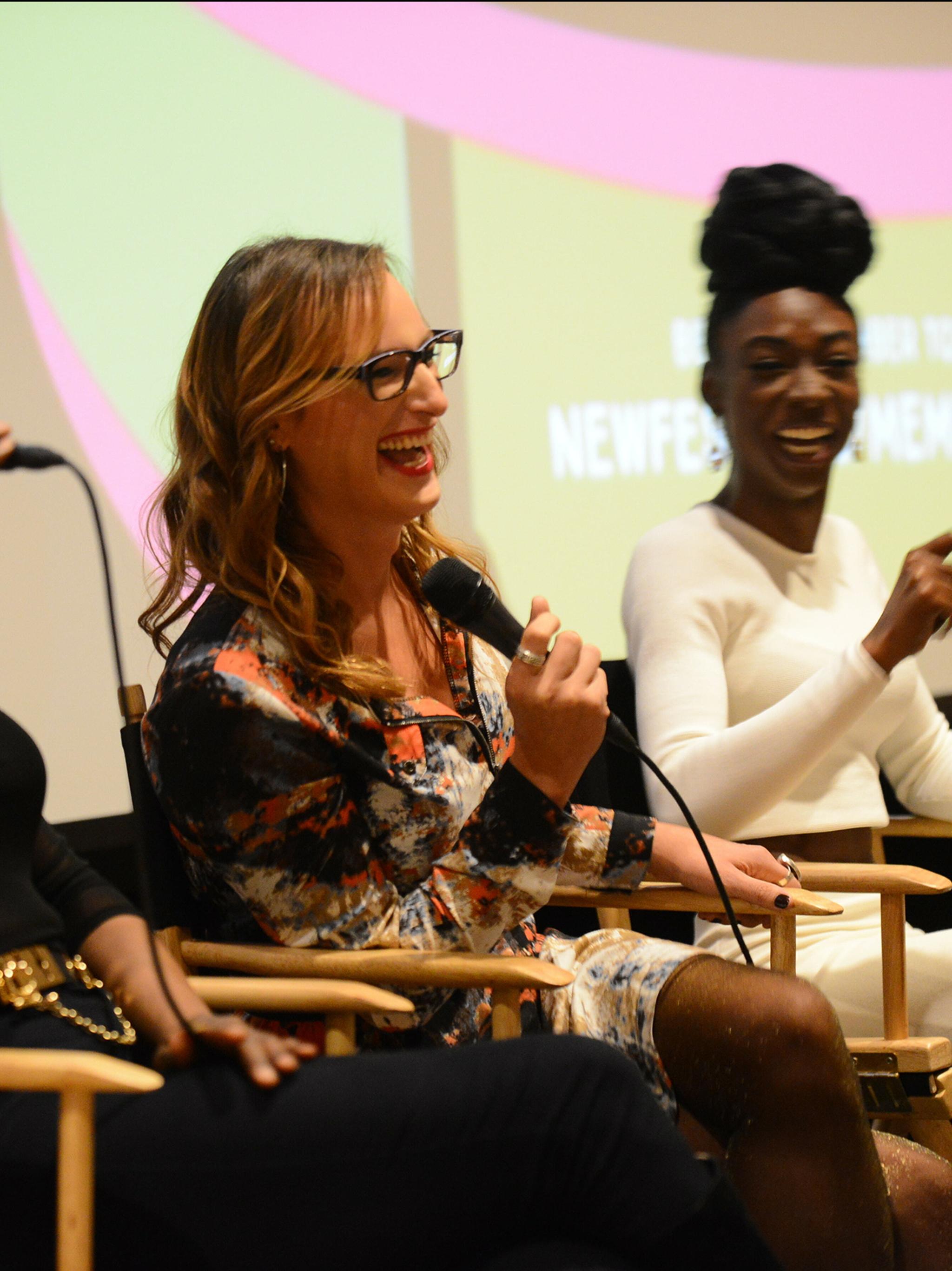 Two panellists laughing with microphones in director chairs at a NewFest event