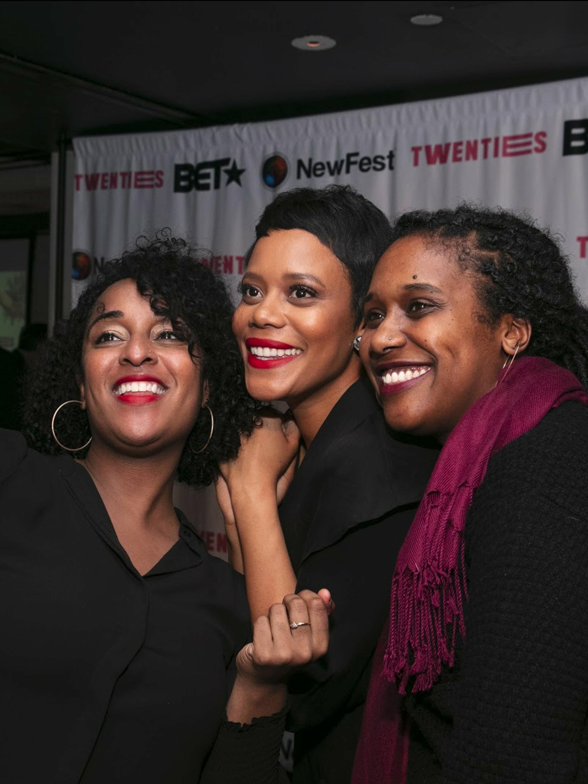 Three attendees smiling at a NewFest step-and-repeat with BET and Twenties branding