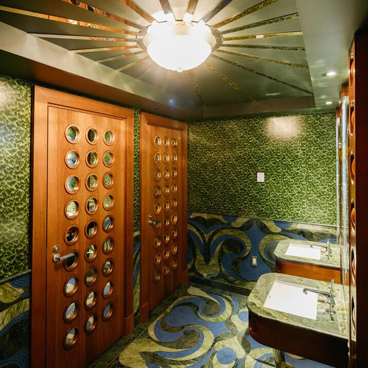 Ornate bathroom with green patterned walls, round-window doors, and two sinks