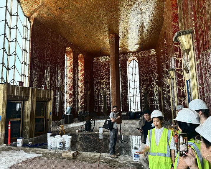 Construction site inside an ornate hall with workers in hard hats and temporary lighting.
