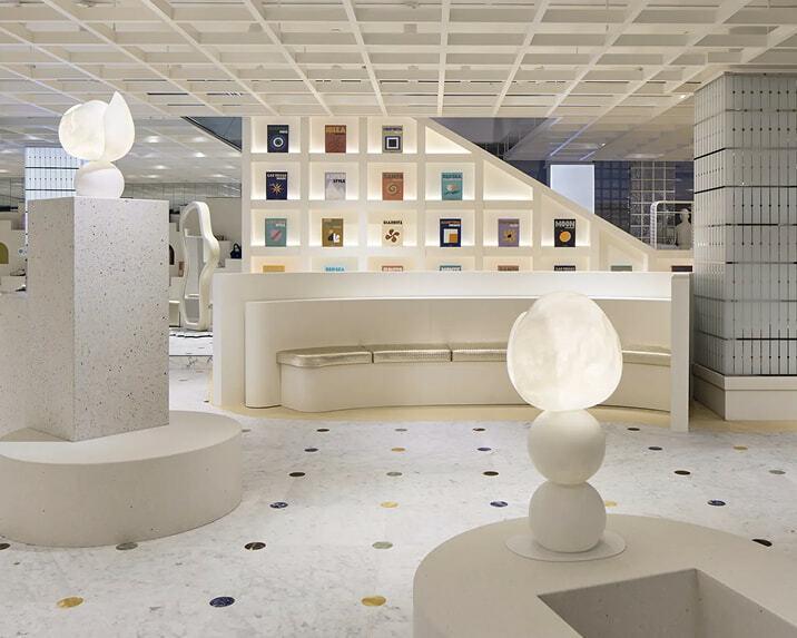 White retail lounge with illuminated sculptures, curved seating, and colorful displays on the wall.
