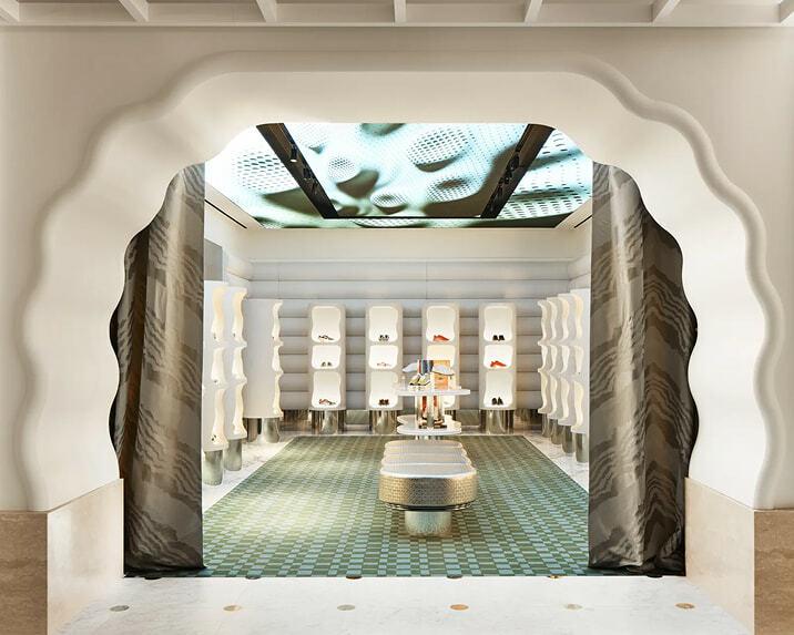Arched retail room with wavy white shelving, patterned green floor tile, and a lit ceiling display.