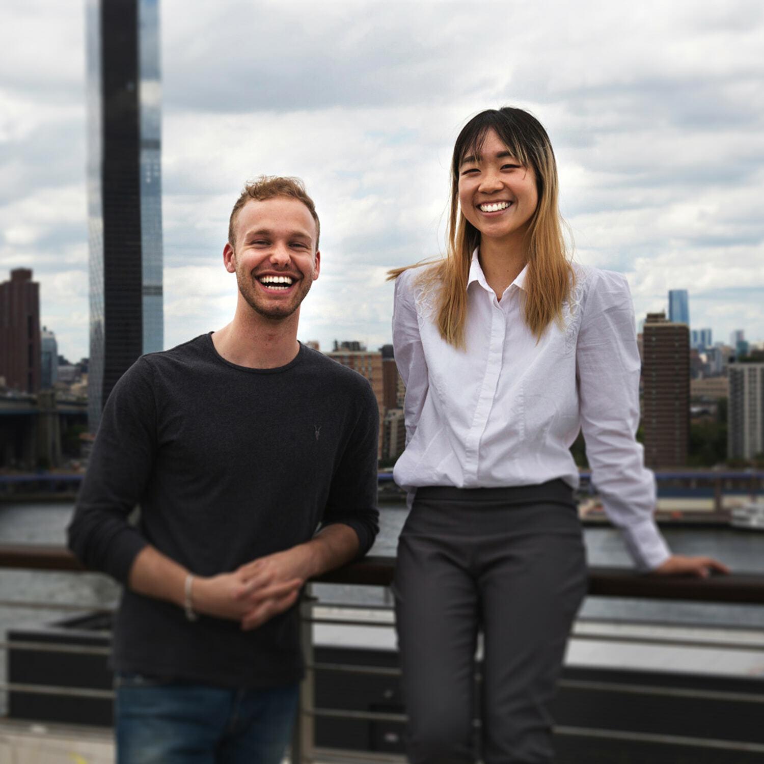 Two people smiling on a rooftop with a city skyline behind them