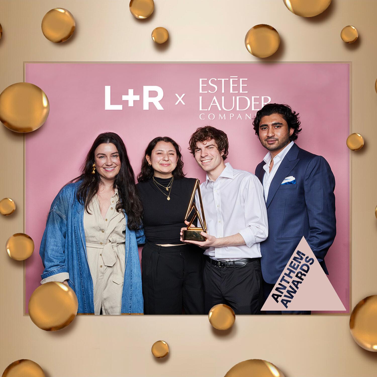 Four people posing with an award at an L+R x Este Lauder Anthem Awards backdrop