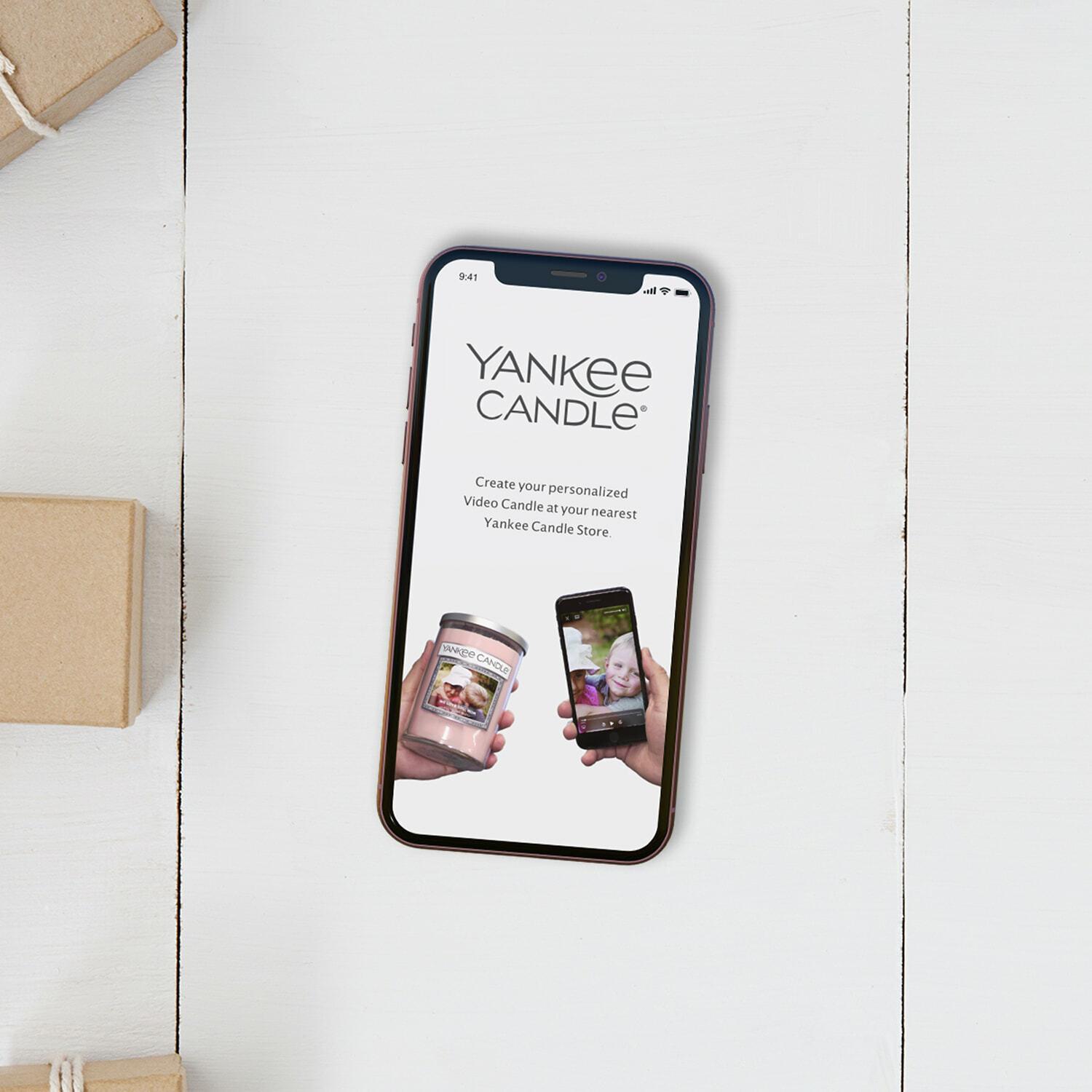 Phone showing the Yankee Candle personalized Video Candle promo beside wrapped gift boxes