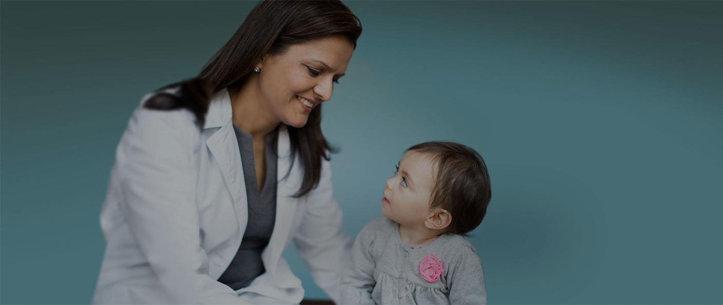 Doctor in a white coat smiling at a baby against a teal background