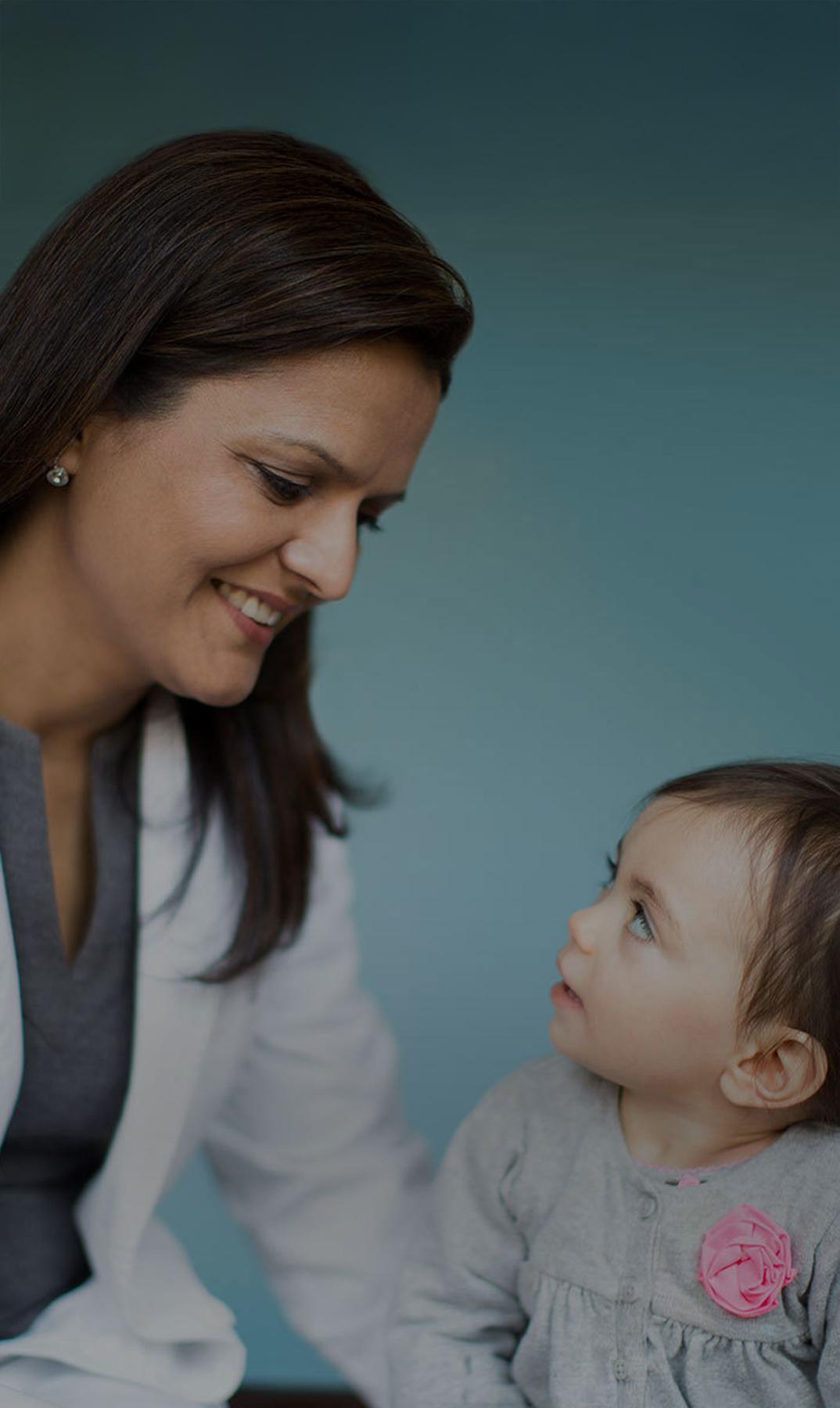 Doctor in a white coat smiling at a baby against a teal background